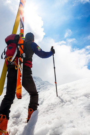  Ski mountaineer walking up along a steep snowy ridge with the skis in the backpack.の写真素材