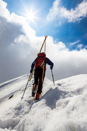  Ski mountaineer walking up along a steep snowy ridge with the skis in the backpack.の写真素材