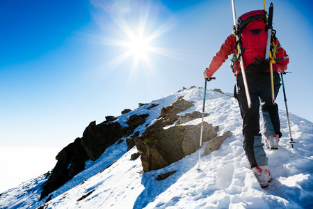 Mountaineer walking up along a steep snowy ridge with the skis in the backpack.の写真素材