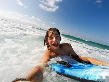 Caucasian male boy enjoys riding the waves with a surfboard. Summer sunny day.の写真素材