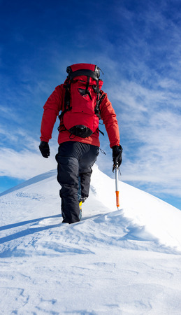 Mountaineer walks on the summit of a snowy peak. Concepts: determination, courage, effort, self-realization. Sunny winter day, european Alps.の写真素材