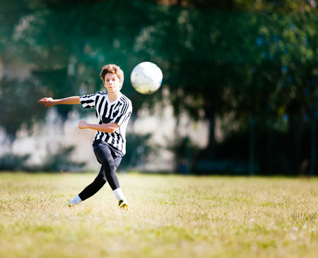 Boy playing football in a soccer field. Caucasian kid dresses a black and white soccer uniform and yellow shoes. Sunny day.の写真素材