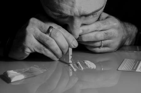 This Caucasian man is snorting cocaine, previously broken into strips, with a rolled up bill. Drug addiction problems. High quality photoの写真素材