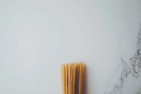 Bunch of dried spaghetti noodles is presented against a plain light gray background. The spaghetti is bundled and is a light beige color.の素材