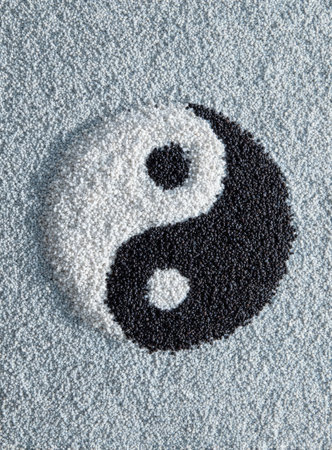 A yin yang symbol is formed from dark and light colored beads on a textured surface.の素材