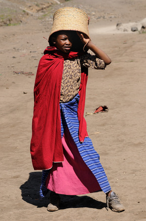 ARUSHA, TANZANIA - MAY 19: African child with woven basket on her head going to the local bazaar in Tanzania, Arusha in May 19, 2013のeditorial素材