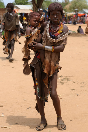 TURMI, OMO VALLEY, ETHIOPIA - JULY 29: Portrait of the of young girl with the child on hands from Hamer people resting under the tree in transit to the local marketplace in Turmi, Omo valley in July 29, 2013のeditorial素材