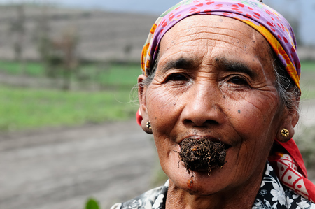 BROMO, JAVA, INDONESIA - MARCH 26: The ethnic woman living in the area of the Bromo volcano is sitting on the volcanic ash with the tobacco in the mouth during the eruption. Bromo on March 26, 2011.のeditorial素材