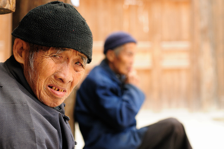 ZHAOXING, CHINA - 11 NOVEMBER 2010:  Old Chinese resting on the doorstep of his cottage in the village Zhaoxingのeditorial素材