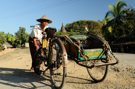 MRAUK-U, MYANMAR - 25 JANUARY 2011: The driver of the rickshaw is pumping the wheel up on a dirt road in Burmaのeditorial素材