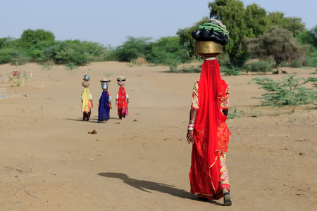 Indian ethnic women carries jar on her head and going for the water in well on the desert. Rajasthan, India. Thar desert near Jaisamlerのeditorial素材