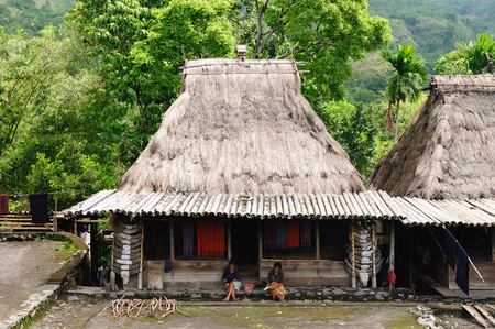 BENA, BAJAWA, INDONESIA - 23 APRIL 2011: Ethnic women sitting on the doorstep traditional grass hut in the Bena minority village on the Flores island near Bajawa.のeditorial素材