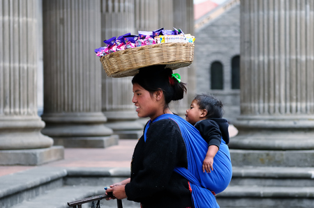 Xela, Quetzaltenango, Guatemala, Central Asia - 24 January 2013: Woman with the child on the back and with basket on the head, is going along streets of the Guatemalan city, relating to historical monuments of the city, so that deploy one's stall and sellのeditorial素材