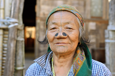 Ziro valley, Arunachal Pradesh, India - 08 JANUARY 2019: Old Apatani woman in front of the house with tribal face tattoo and black wooden nose plugs, to make them less appealing. The Apatanis living in the Ziro valley in the Himalaya in Northeast Indiaのeditorial素材