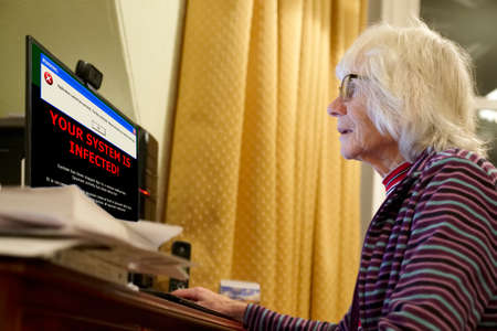 Old elderly senior person with virus warning on computer monitor screenの写真素材