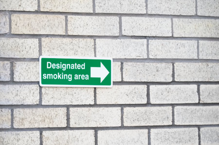 Designated smoking area direction arrow sign on wallの写真素材
