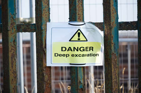 Deep excavations danger sign on fence with trench hole in background on construction site