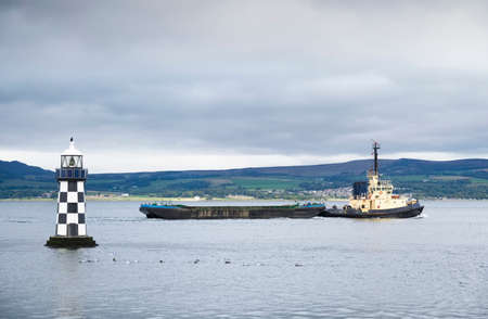 Tugboat transporting floating storage container platform and lighthouseの写真素材