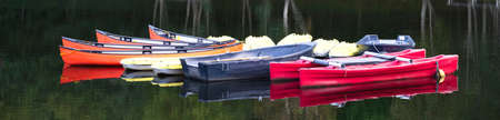 Red blue and yellow kayak canoes in row moored at lakeの写真素材