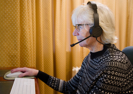 Senior elderly lady using headset earphones and microphone to talk to family on a computerの写真素材
