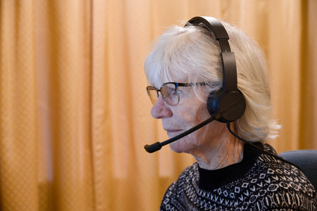 Senior elderly lady using headset earphones and microphone to talk to family on a computerの写真素材