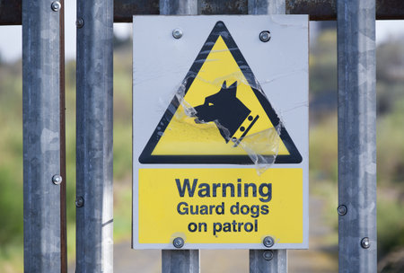 Guard dogs on patrol warning sign on security fence at construction siteの写真素材