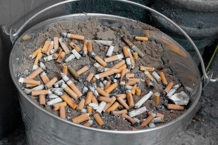 cigarettes stubbed out in bucket of sand outside pubの写真素材