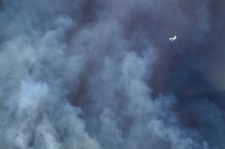 White Aircraft Flying Ahead of the Dense White Smoke Rising from the Raging Wildfireの写真素材