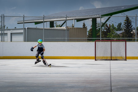 Calgary Alberta Canada, July 09 2022: A young boy playing roller hockey skating at a new outdoor rink in the community of Hawkwood with a solar rooftop amphitheater at background.のeditorial素材
