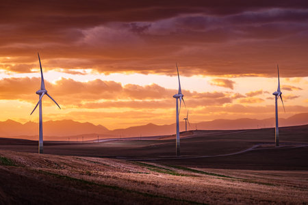 Windmills at sunset generating electricity overlooking distant mountains over agriculture fields...