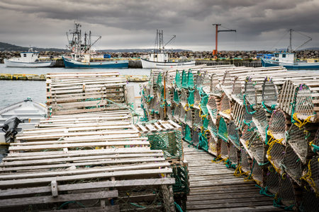 Whiteway Newfoundland Canada, September 25 2022: Wooden lobster traps neatly stacked on a dock with fishing boats at background at a small Maritime community vacation destination.のeditorial素材