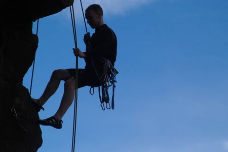 Silhouette of male rock climber hanging from ropes.の写真素材