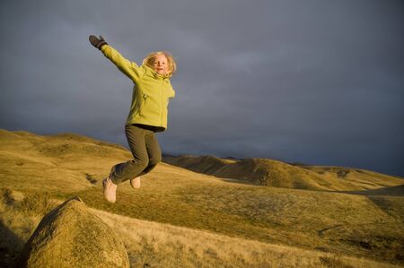 Little girl jumping from a rock in beautiful sunset lightの写真素材