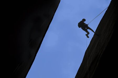 Silhouette of rock climber rappelling a crack with blue sky behind.