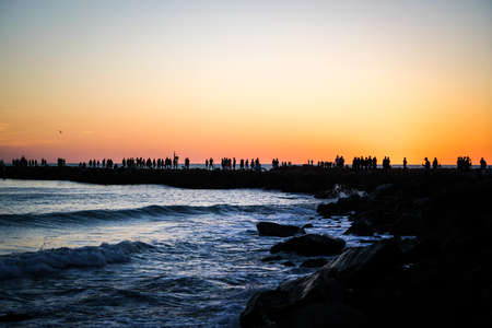 A warm orange sunset at the Jetty in Venice with dark silhouettes cast against the setting sun.の写真素材
