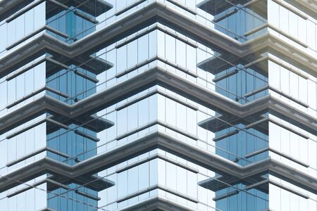 Abstract closeup of the glass-clad facade of a modern building covered in reflective plate glass.