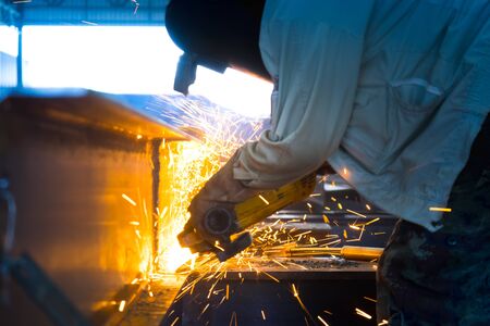 Heavy industry worker cutting steel structure with angle grinding in factory.