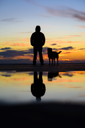 Silhouette of man with his dog at sunset on backgroundの写真素材