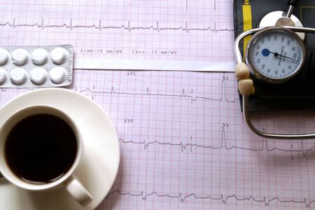 Hemopiezometer for measuring blood pressure, cup of coffee, pills and ECG test results on the table