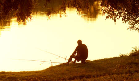 Fisherman with fishing rods in the evening at sunset. Rest after a hard working week. The excitement of a successful catch.の写真素材