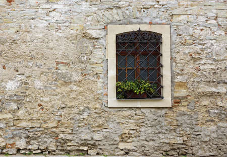 Wooden window with flowers on windowsill on stone wall of ancient house. Background with free space for text.の写真素材