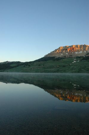 Mountain landscape reflecting in crystal clear lake waters during sunrise.
