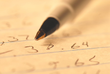 A close angle image of a ball point pen and numbers on paper.