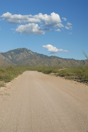 A gravel and dirt path leading into the mountains in southern Arizona, with a blue sky and puffy white clouds.の写真素材