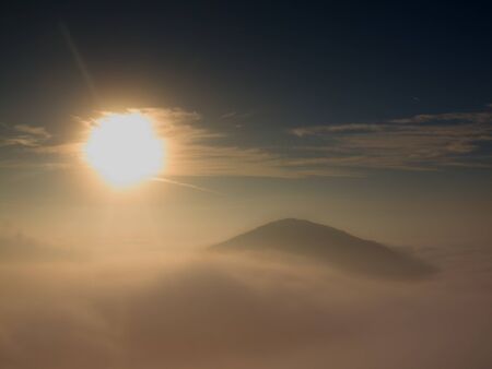 Magnificent heavy mist in landscape. Autumn fogy sunrise in a countryside. Hill increased from fog, the fog is colored to golden and orange.の写真素材