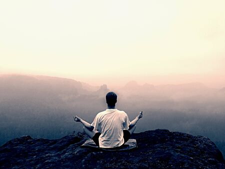 Man is doing Yoga pose on the rocks peak within misty morningの写真素材