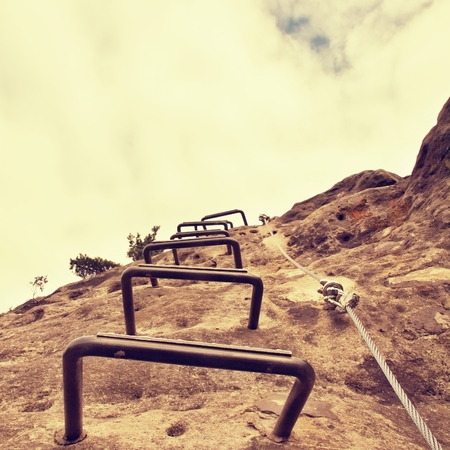 Iron cramps in rock, tourist ladder. Iron twisted rope fixed in the block by screws snap hooks. The rope end anchored into sandstone rock. Climbers way.の写真素材