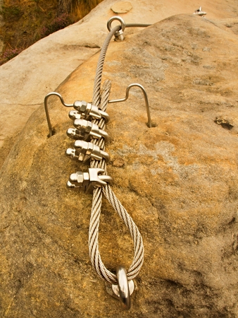 Iron twisted rope fixed in block by screws snap hooks. Detail of rope end anchored into rock
