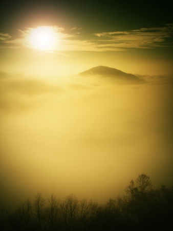 Magnificent heavy mist in landscape. Autumn fogy sunrise in a countryside. Hill increased from fog, the fog is colored to golden and orange.の写真素材