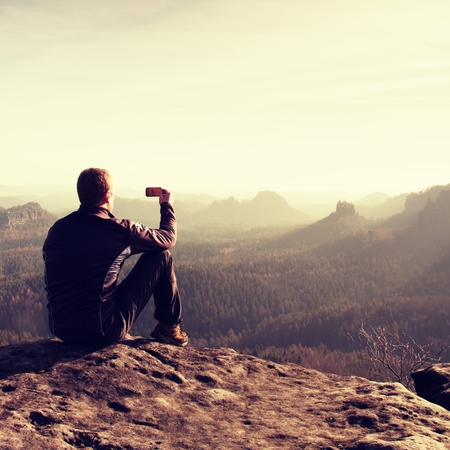 Hiker is taking photo by smart phone on the peak of mountain  at sunrise.の写真素材